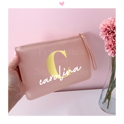 Pochete rosa claro com letra C amarela e texto carolina branco perto de jarro com flores cor de rosa