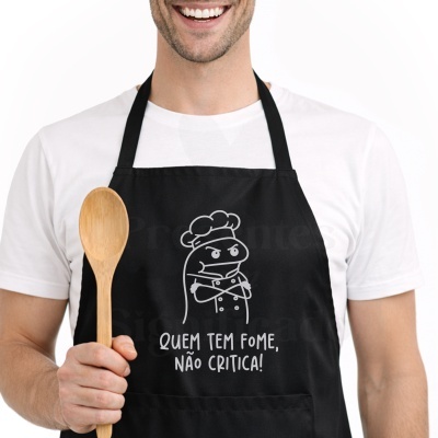 Avental preto com desenho de chef e frase em português usado por pessoa com colher de pau