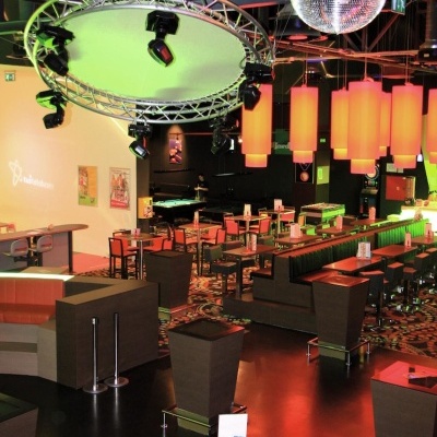 Interior de bar com iluminação laranja, espelho de bola de discoteca e móveis escuros