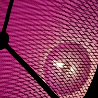 Luminária com estrutura metálica preta, malha cor-de-rosa e lâmpada interna visível