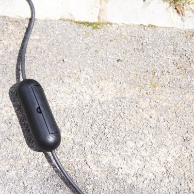 Interruptor preto em cabo sobre cimento cinza com muro de pedras