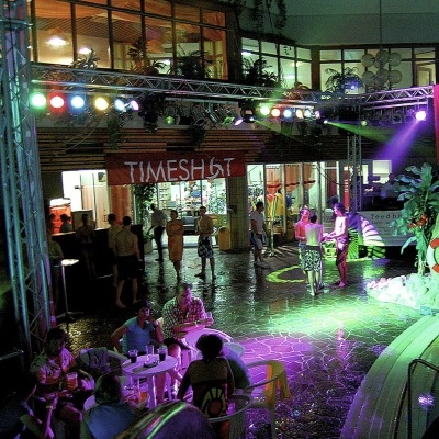 Área recreativa com mesas coloridas, luzes e logo TIME SHOT