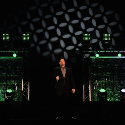 Palco iluminado com luzes verdes e roxas e padrão de luz circular no fundo