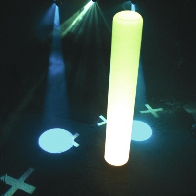 Coluna luminosa branca cilíndrica em ambiente escuro com luzes de palco azuis e verdes