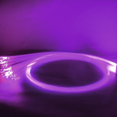 Cabo de fibra ótica que emite luz roxa, com várias fibras finas e caixa preta numa superfície plana