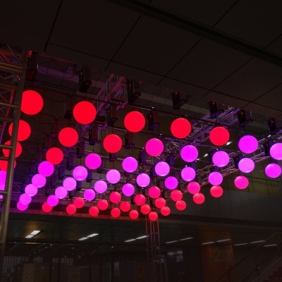 Estrutura metálica com esferas luminosas vermelhas e roxas suspensas no teto de um espaço interior