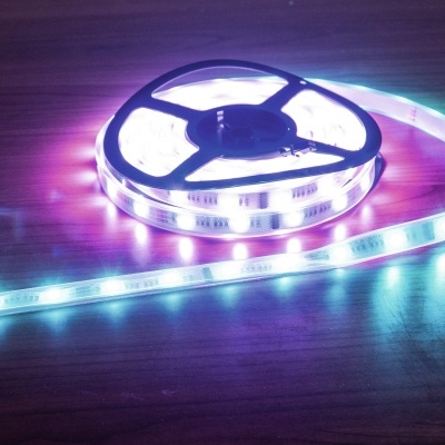 Fita LED flexível azul, roxa e branca enrolada em bobina preta numa superfície de madeira