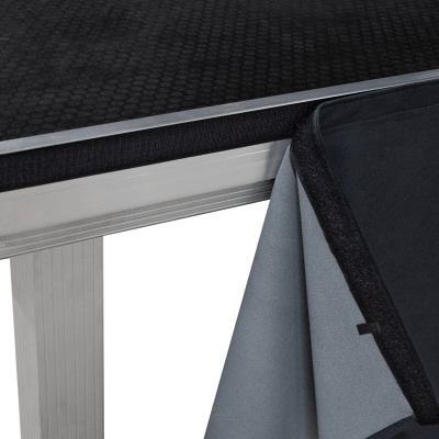 Mesa com tampo preto e estrutura metálica prateada com tecido na borda e pano cinza pendurado na lateral.