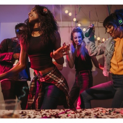 Quatro jovens a dançar em festa interna com roupa casual e fones de ouvido iluminados