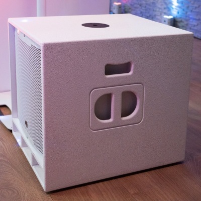 Subwoofer branco com textura rugosa em chão de madeira e parede iluminada ao fundo