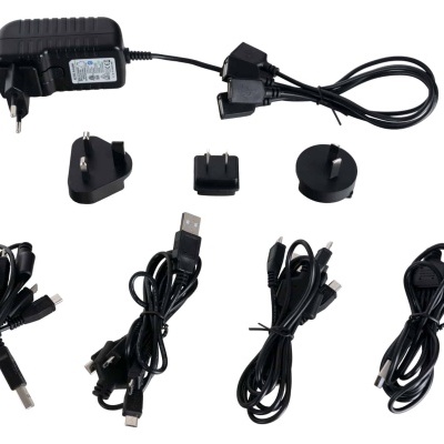 Adaptadores de corrente e cabos USB pretos com vários tipos de plugues e conectores, sobre fundo branco.