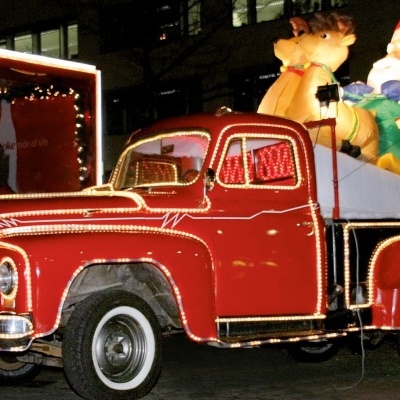 Camião pick-up vermelho decorado com luzes de Natal e figuras insufláveis de Pai Natal e rena