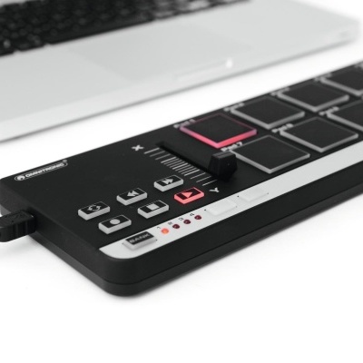 Controlador MIDI preto com botões e botão rosa ao lado de portátil prateado