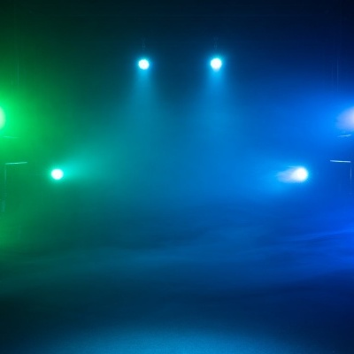 Luzes coloridas verdes, azuis e brancas iluminando um ambiente escuro e nebuloso