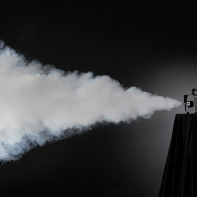 Máquina de fumo preta a emitir fumo sobre suporte preto em fundo escuro