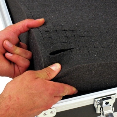 mãos a cortar bloco de espuma preta dentro de caixa de transporte metálica