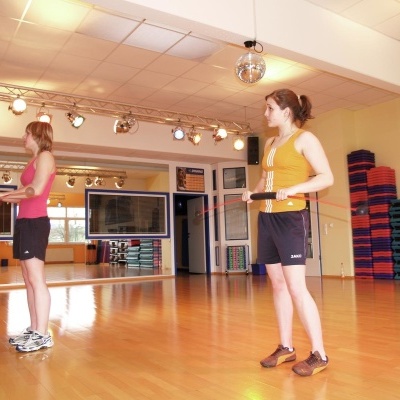 Duas mulheres em sala de ginástica vestindo calções pretos com tops de cores diferentes.