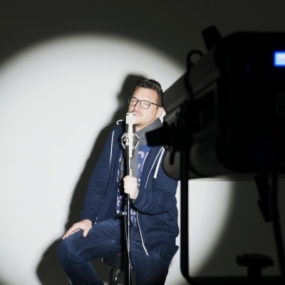 Homem sentado com microfone iluminado por holofote branco