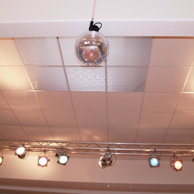 Teto com painel branco quadrado, esfera de discoteca prateada pendurada e luzes coloridas de palco