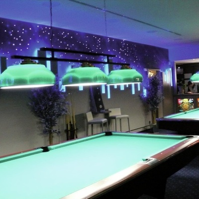 Sala de bilhar com mesas verdes e luzes pendentes verdes