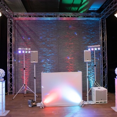Estrutura metálica iluminada com colunas de luzes, altifalantes e painel branco no interior