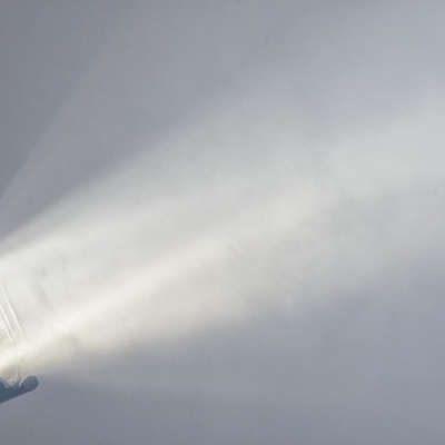 Projetor preto emitindo feixe de luz branco em ambiente nevoento