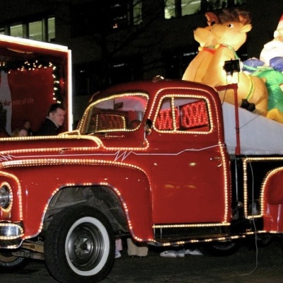 Carrinha vermelha com decorações de Natal iluminadas e figuras infláveis de Pai Natal e rena à noite