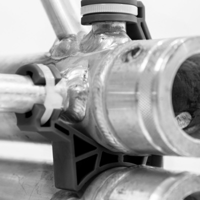 Junções de tubos metálicos com suportes plásticos pretos em fundo branco.