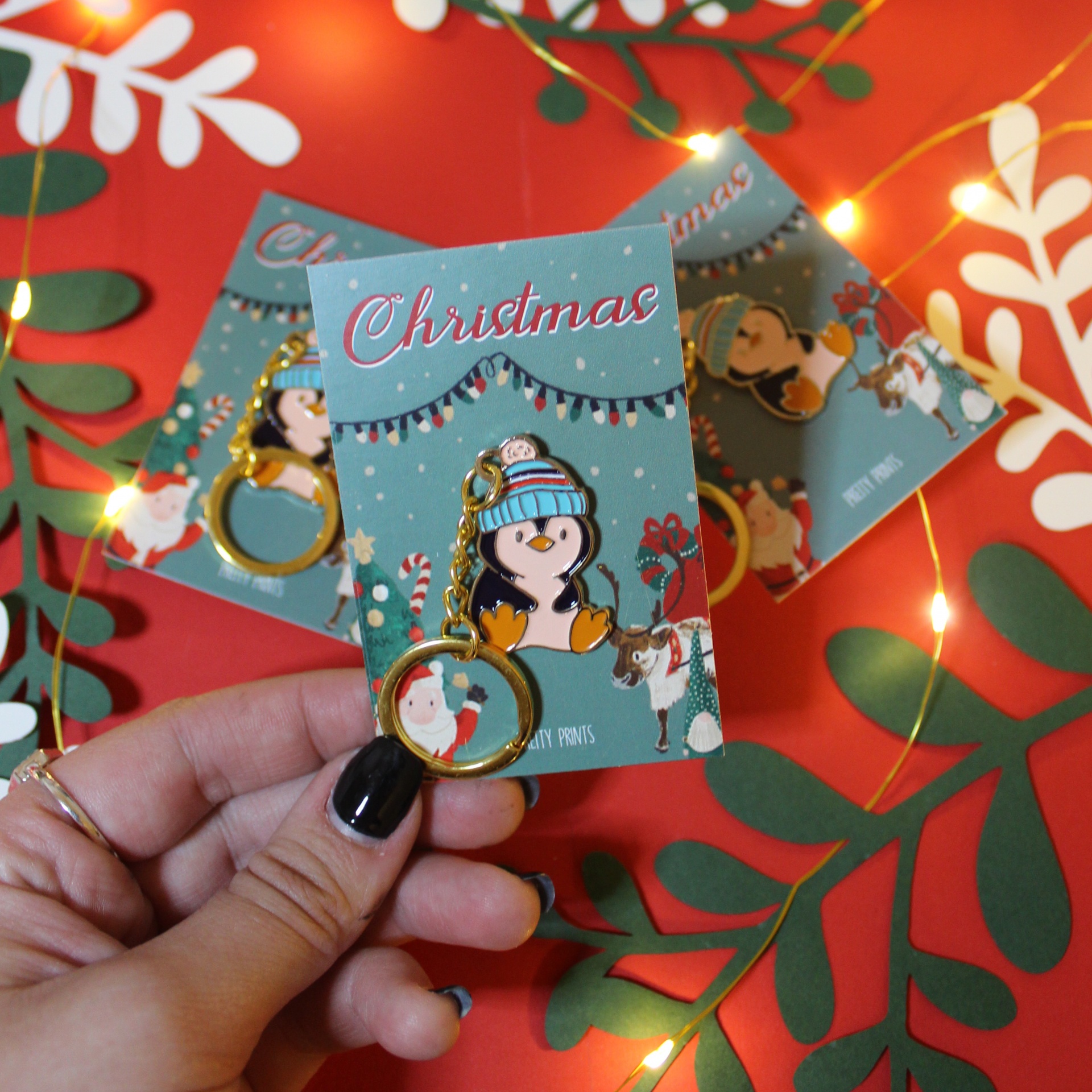 Chaveiros de pinguim em cartão de natal com fundo vermelho e padrões verdes e brancos.