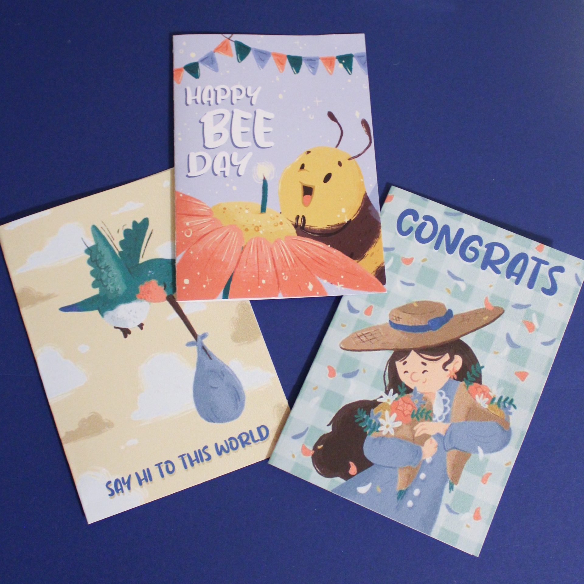 Três cartões coloridos ilustrados com abelha, beija-flor e menina, com textos em inglês, sobre fundo azul.