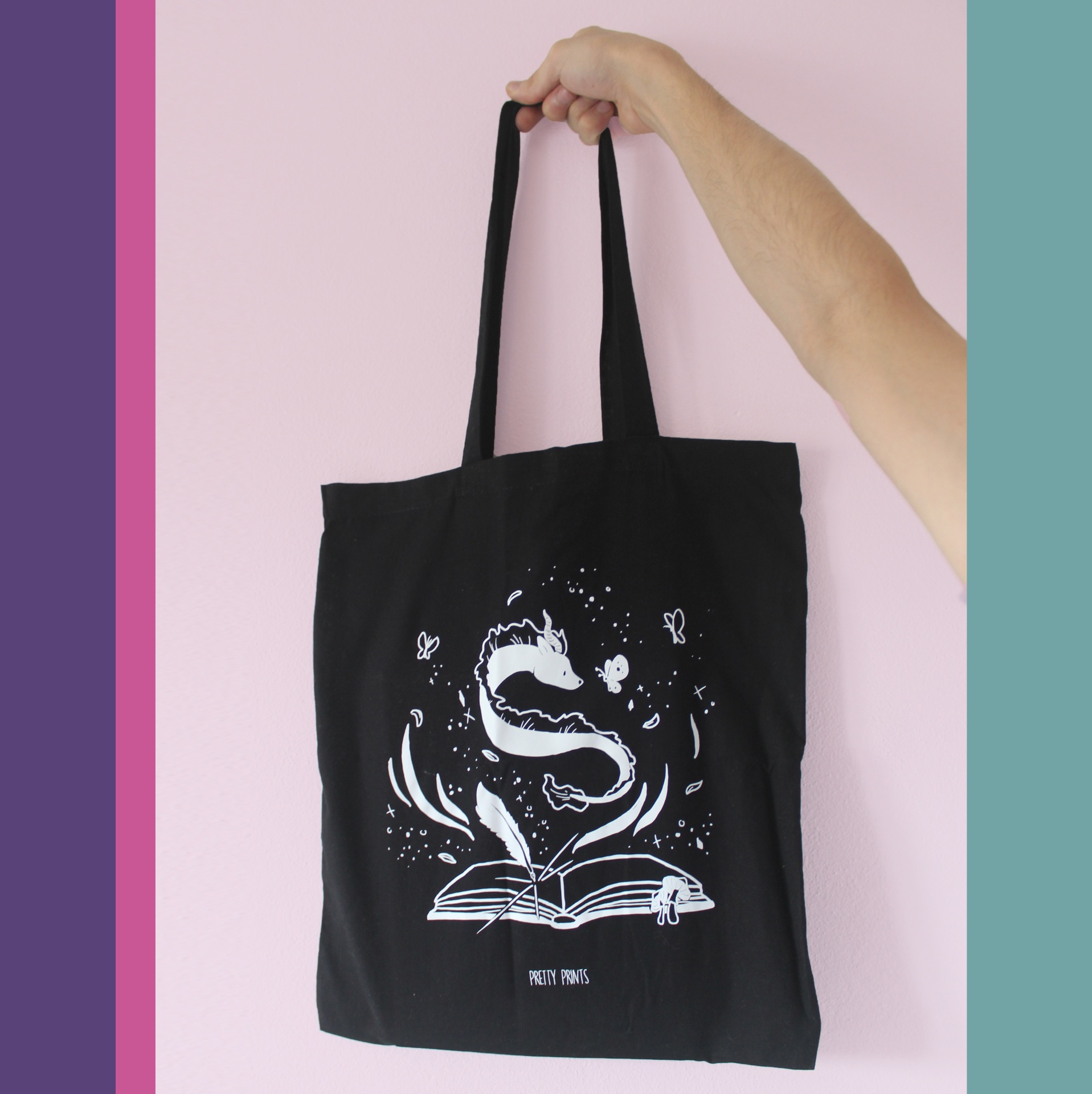 Mala preta de pano com alças e desenho branco de livro aberto e elementos mágicos