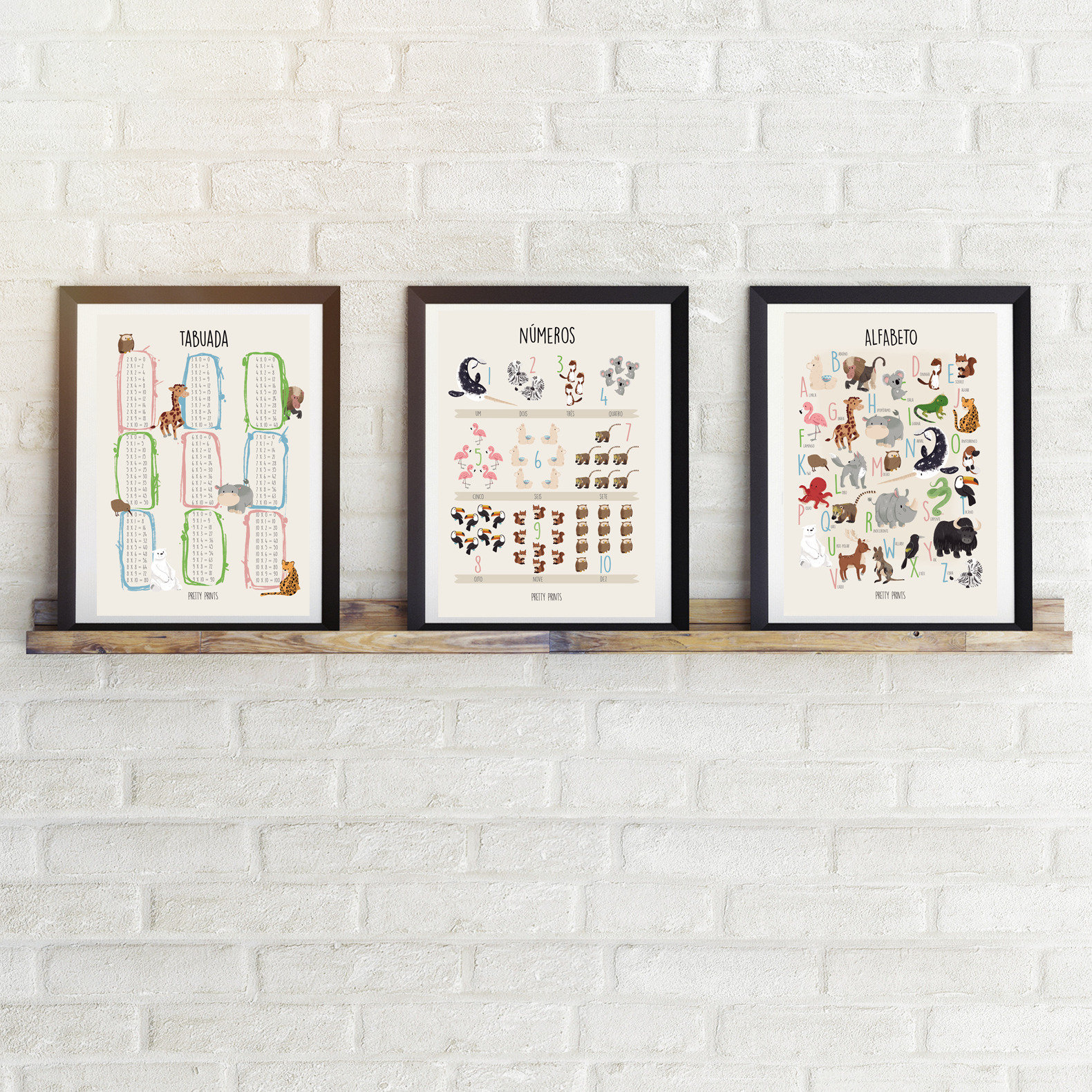 Três quadros educativos com temas de tasquara, números e alfabeto, com ilustrações coloridas, sobre prateleira de madeira contra parede branca de tijolos
