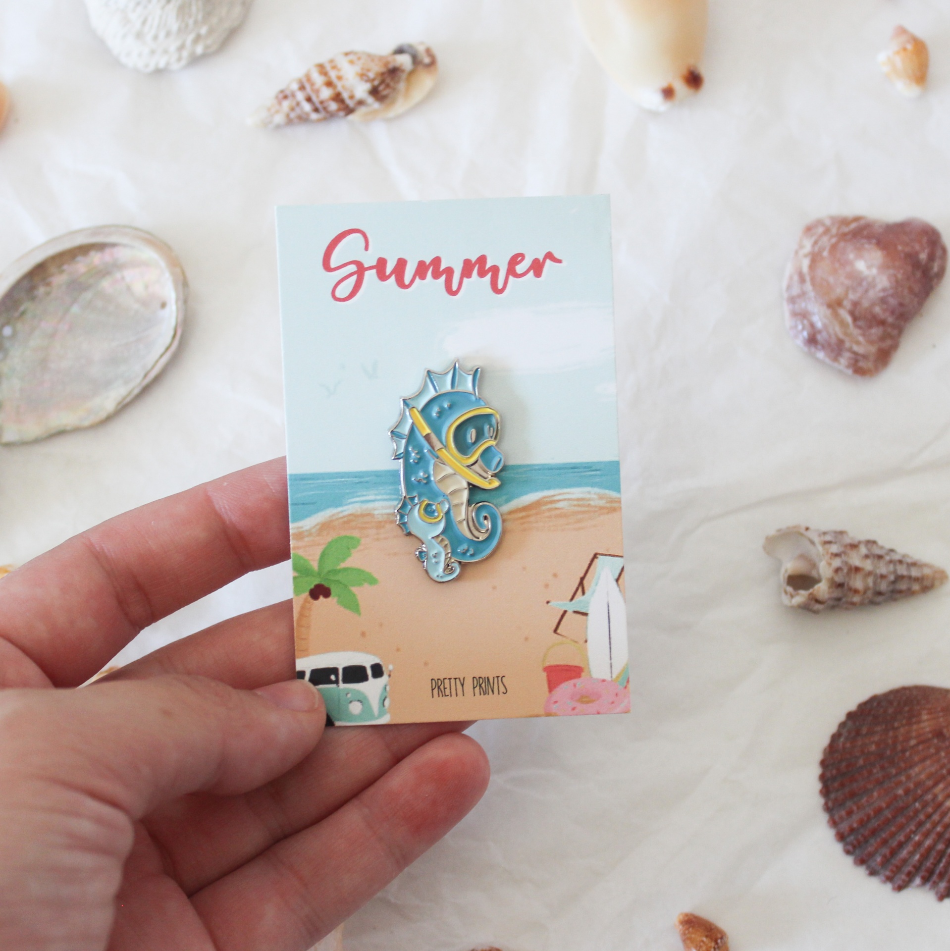 Broche cavalo-marinho azul com cartão ilustrado de praia e conchas ao redor