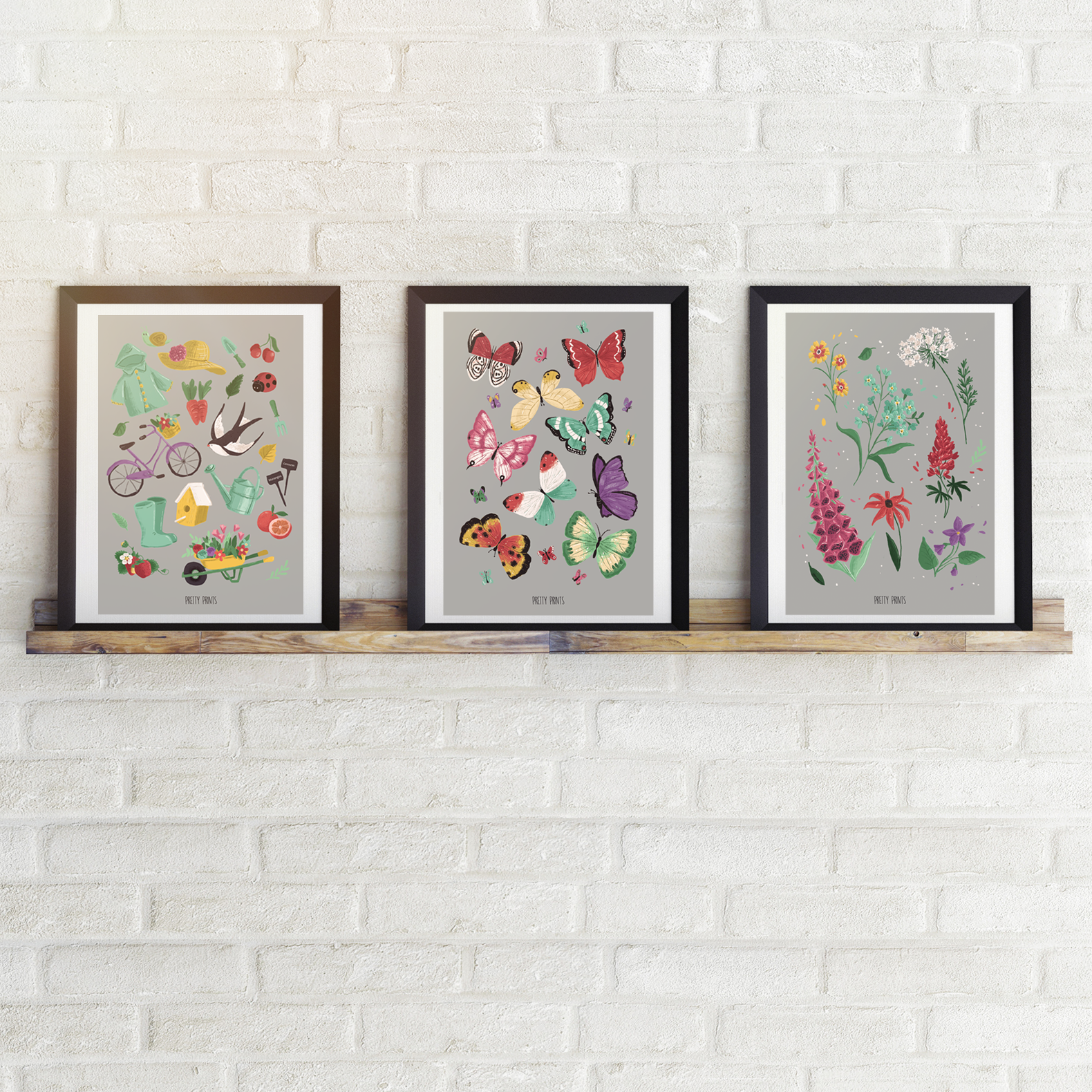 Três quadros coloridos com desenhos de bicicletas, borboletas e flores emoldurados numa prateleira frente a parede branca