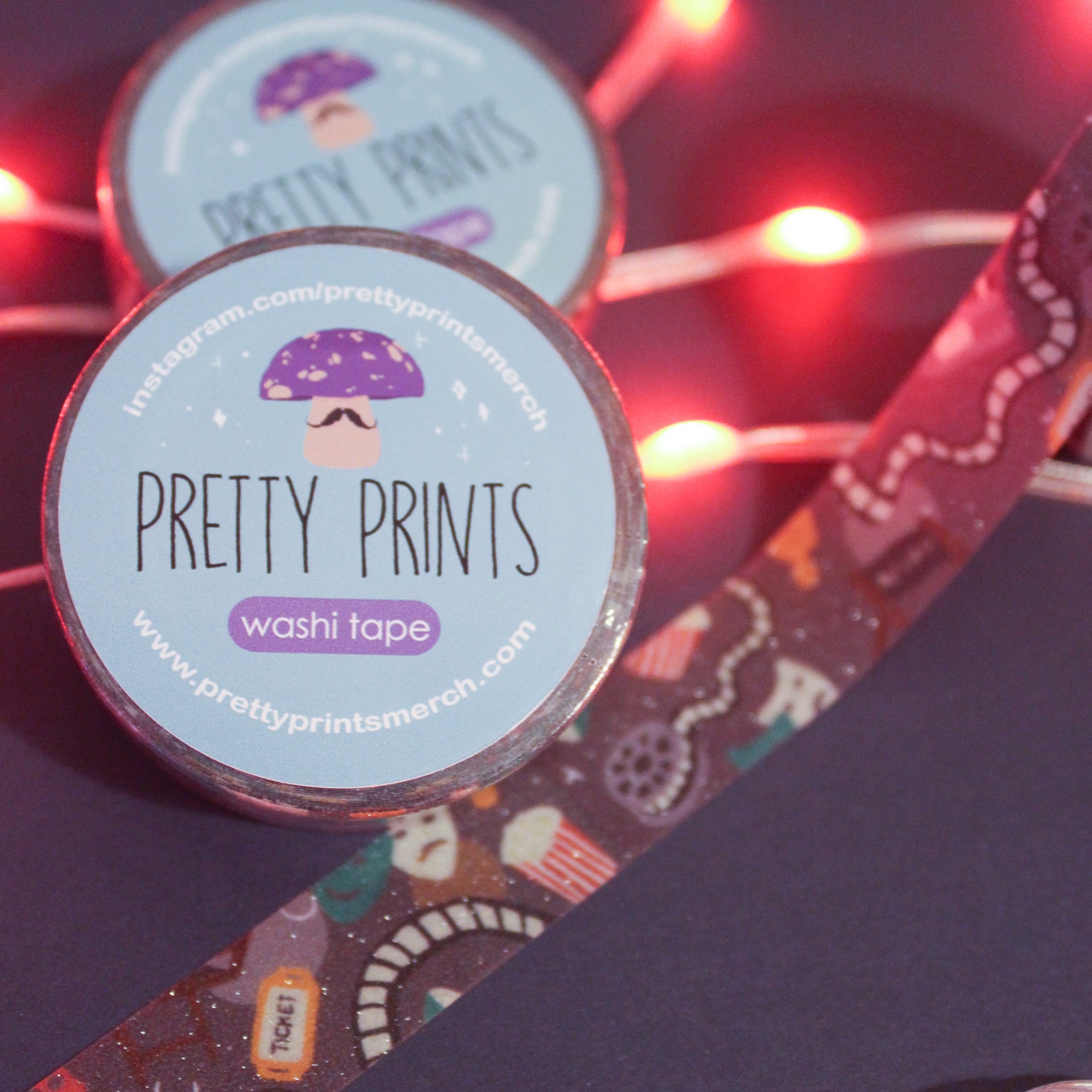 Rolo de washi tape decorativa com padrão colorido e etiqueta azul em fundo escuro com luzes vermelhas