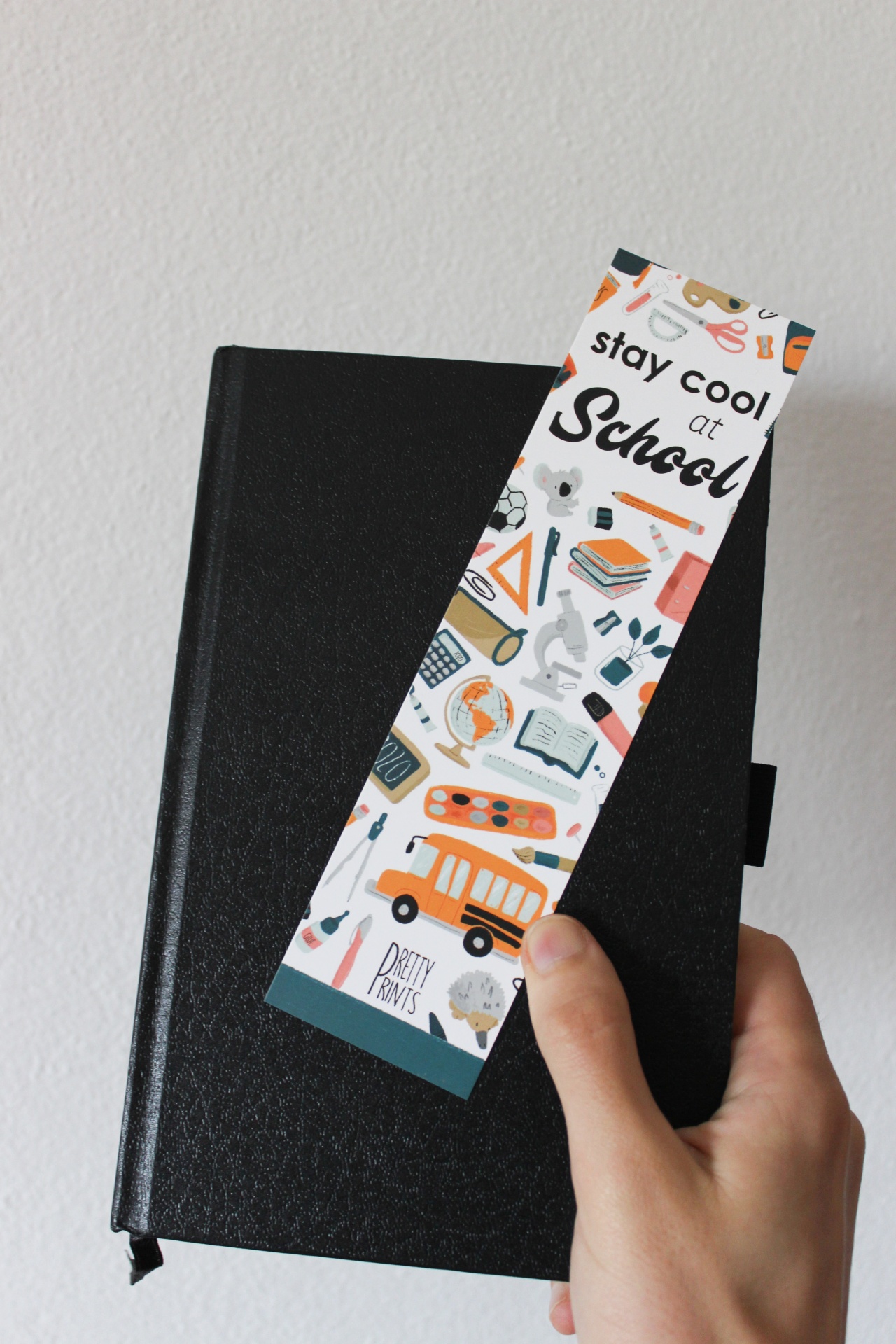 Marcador de livros colorido com texto stay cool at School sobre livro preto.