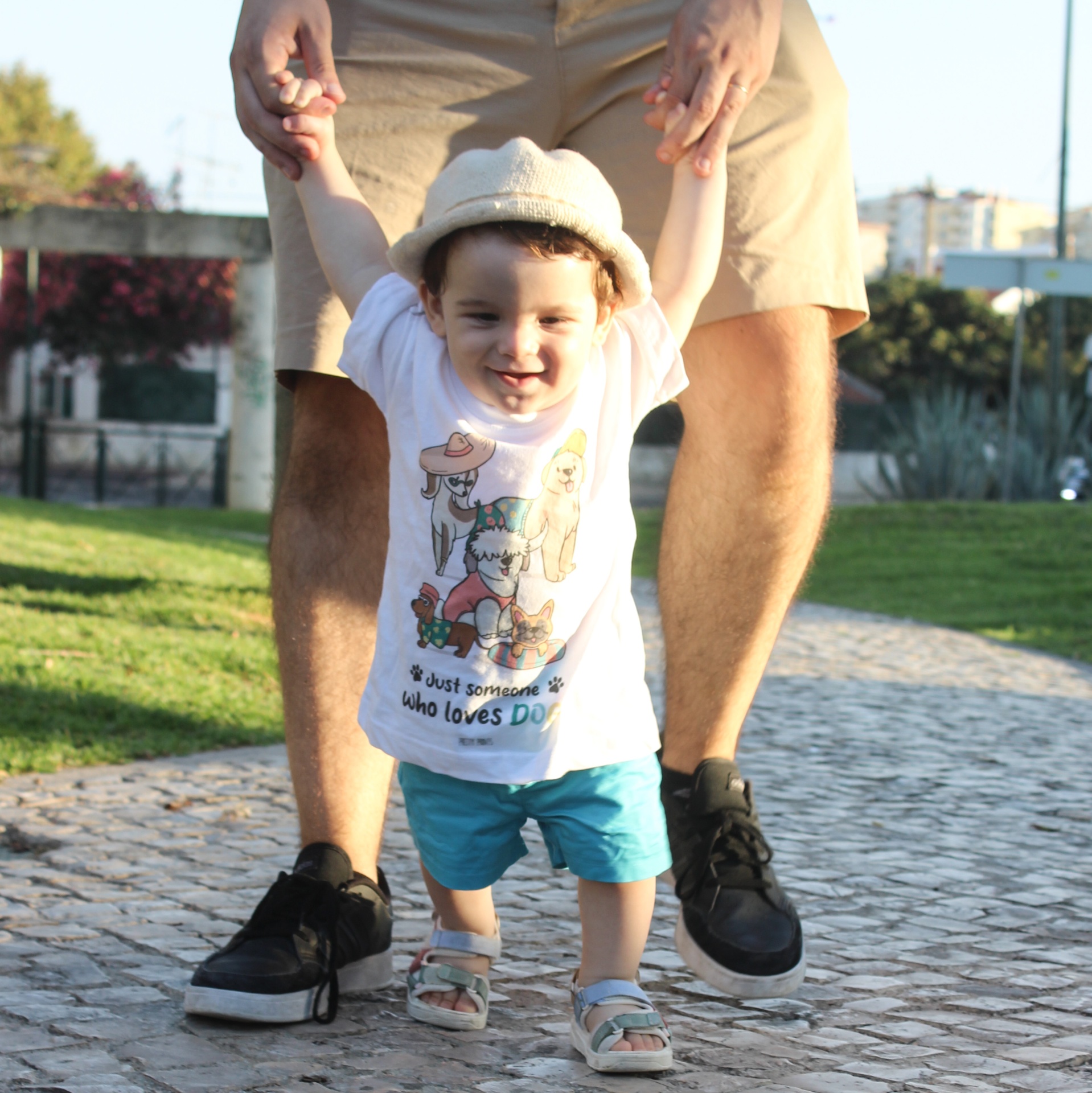 Criança com t-shirt branca e chapéu a caminhar com ajuda de adulto