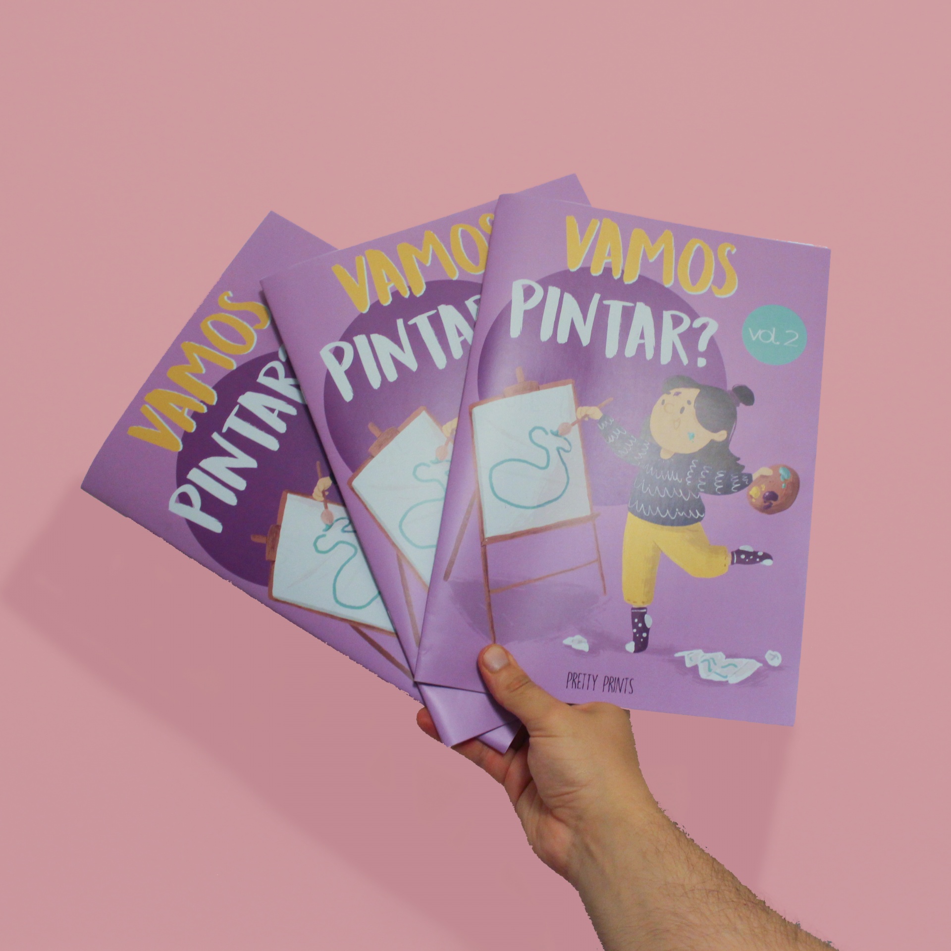 Três livros VAMOS PINTAR? vol.2 com capa roxa e ilustração de criança a pintar num fundo rosa