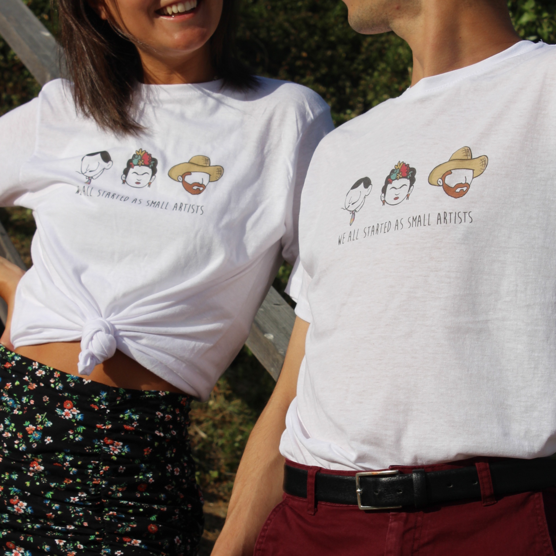 T-shirts brancas com desenhos de rostos e texto WE ALL STARTED AS SMALL ARTISTS