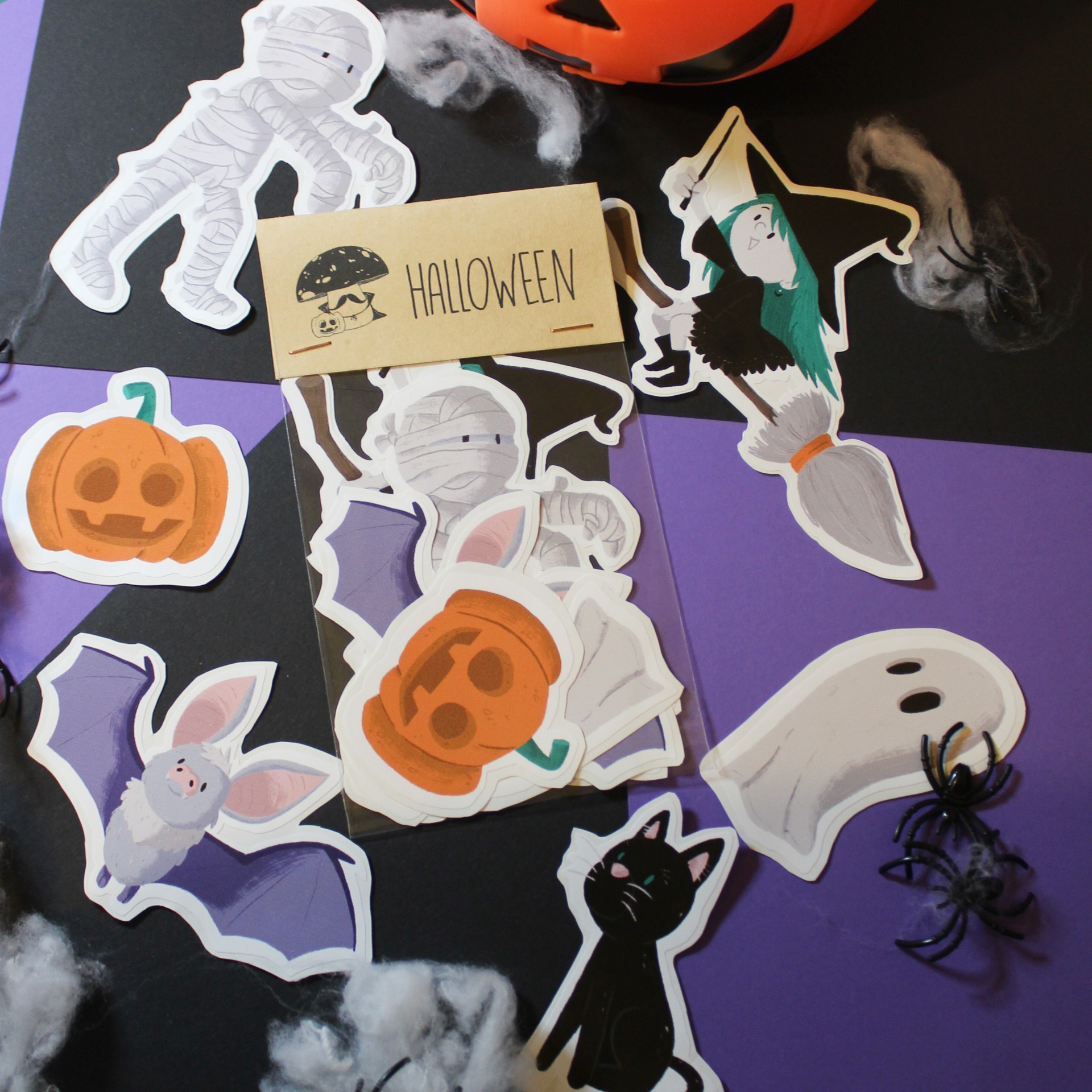 Recortes em papel de personagens de Halloween sobre fundo preto e roxo com teias e aranhas falsas