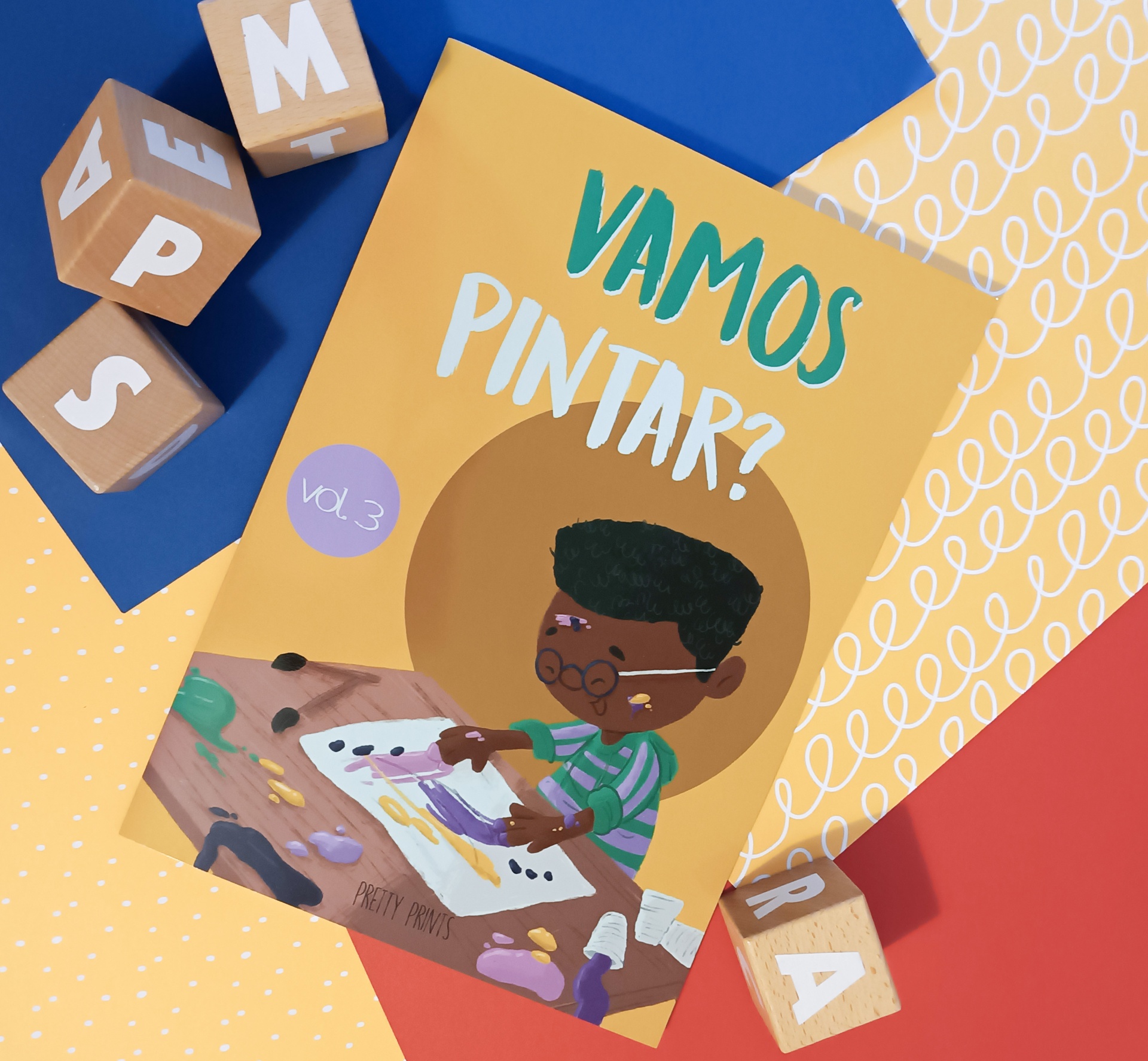 Livro infantil 'VAMOS PINTAR?' com criança a pintar e cubos de madeira coloridos ao redor