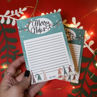 Bloco de notas Merry Notes com decoração natalícia e linhas para escrita segurado por mão feminina