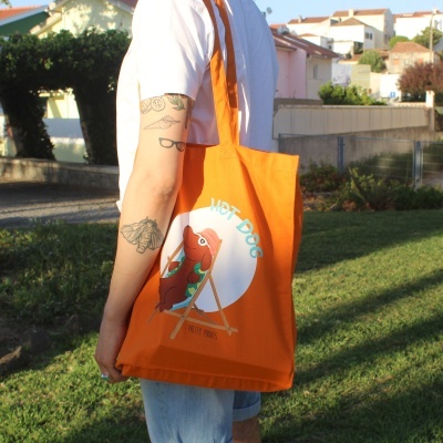 Saco de tecido laranja com desenho de cachorro em espreguiçadeira e texto 'HOT DOG'