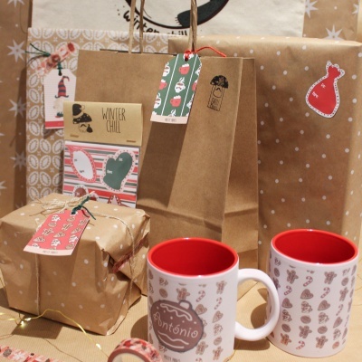 Canecas brancas com interior vermelho e presentes embrulhados em papel castanho com etiquetas de Natal