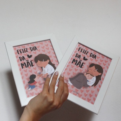 Dois quadros de madeira branca com ilustrações mãe e filha e texto 'FELIZ DIA DA MÃE' em fundo rosa com corações.