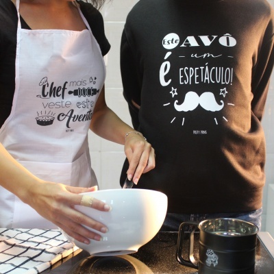 Pessoa com avental branco a mexer numa tigela branca e outra pessoa ao lado com t-shirt preta estampada