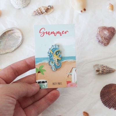Broche cavalo-marinho azul com cartão ilustrado de praia e conchas ao redor