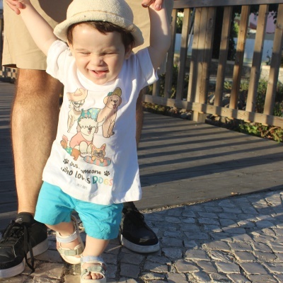 Criança a caminhar com t-shirt branca e calções azuis numa calçada de pedra