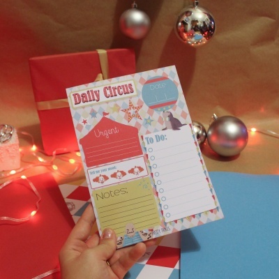 Folha 'Daily Circus' colorida com listas e ilustrações, decoração de Natal com bolas e presente ao fundo