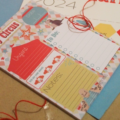 Bloco de notas colorido com secções para escrever, decorado com palhaços e estrelas.